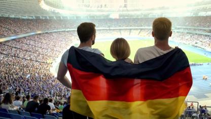 Fußball-Europameisterschaft 2024 - Menschen mit Deutschland-Flagge stehen im Fußballstadion