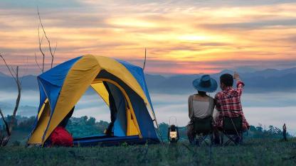 Zelten in der Natur - Paar sitzt neben seinem Zelt bei Sonnenaufgang