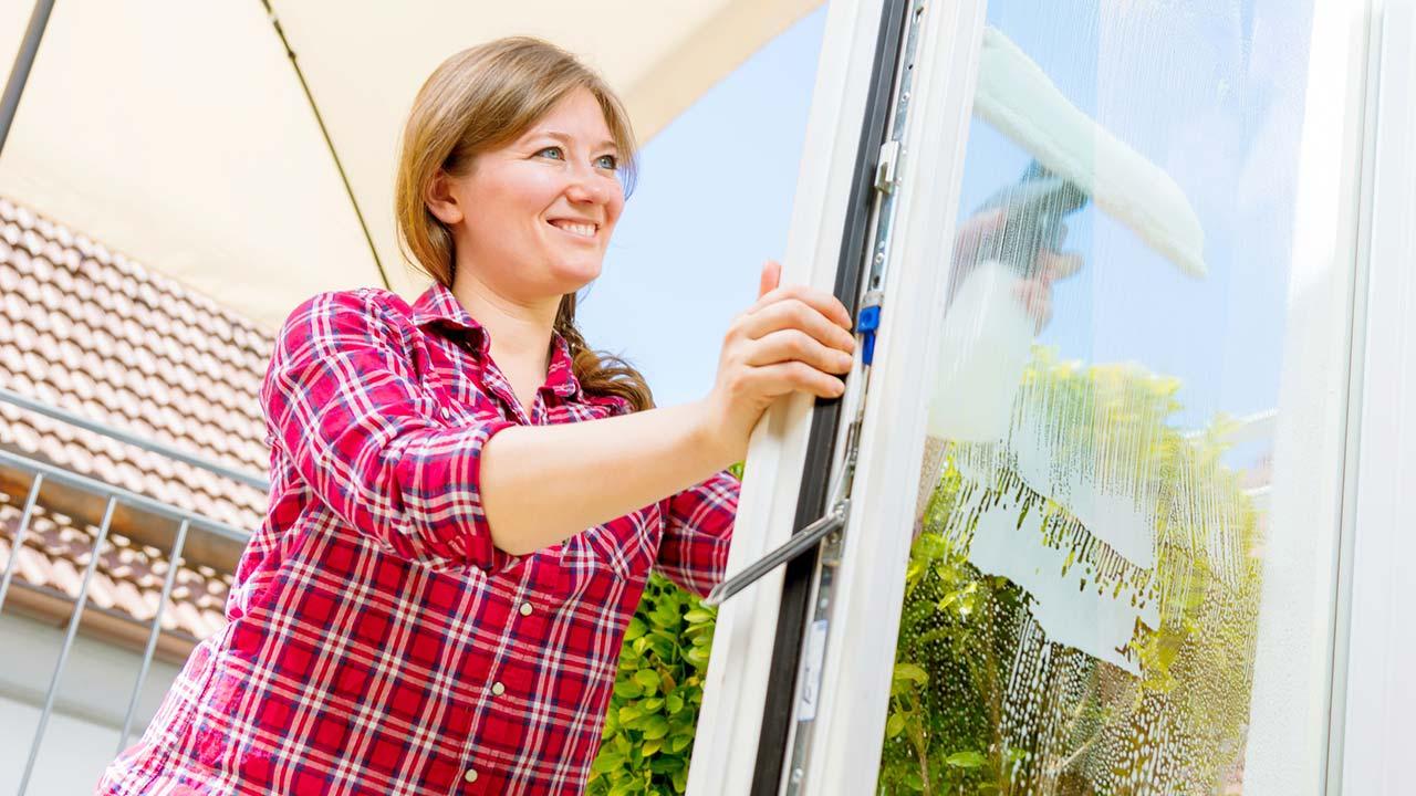 Fenster einfacher putzen mit Fenstersauger - Frau putzt im Sonnenschein