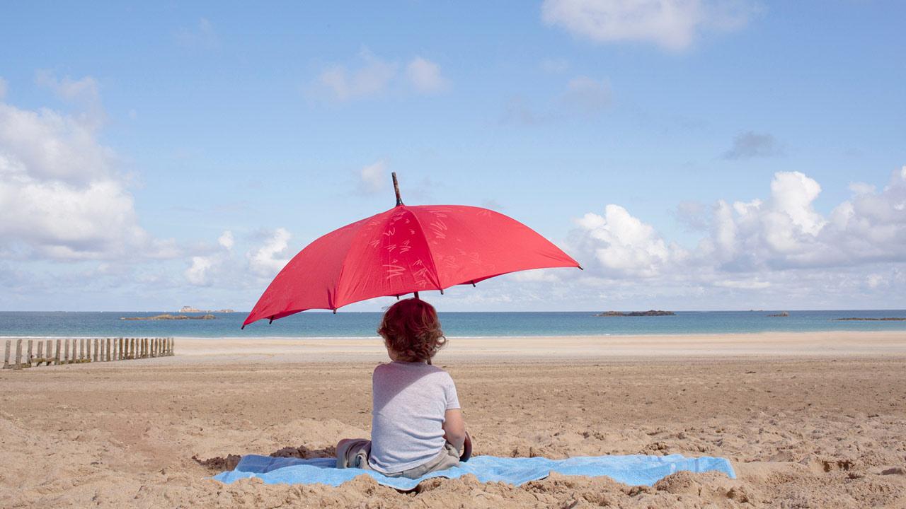 Der passende Sonnenschutz für mein Kind / ein kleines Kind sitzt unter einem Sonnenschirm